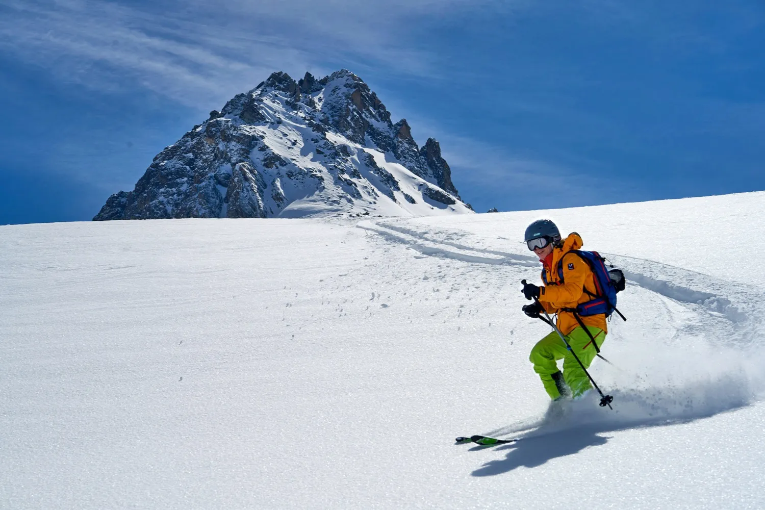Person fährt Ski im Schnee neben verschneitem Berggipfel.